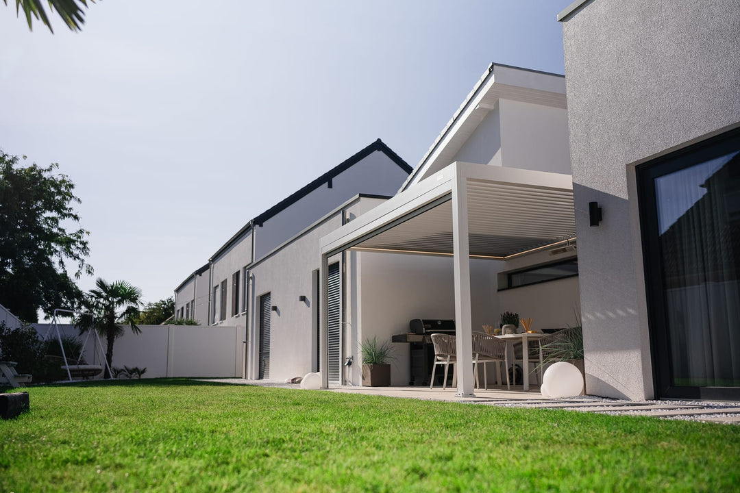 Pergola bioclimatique aluminium avec lames ouvertes sur terrasse française ensoleillée, comparée à une véranda vitrée en arrière-plan