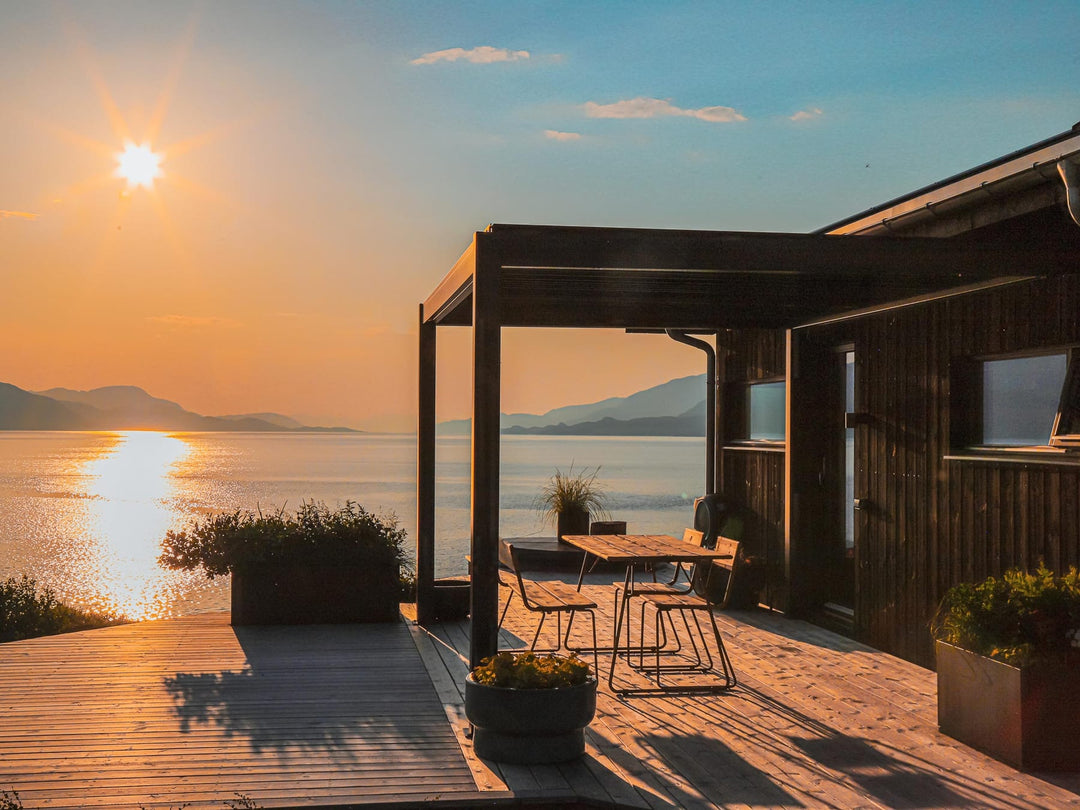 Pergola 4 Pro en aluminium anthracite sur terrasse française, lames à mi-ouverture sous ciel nuageux d'automne
