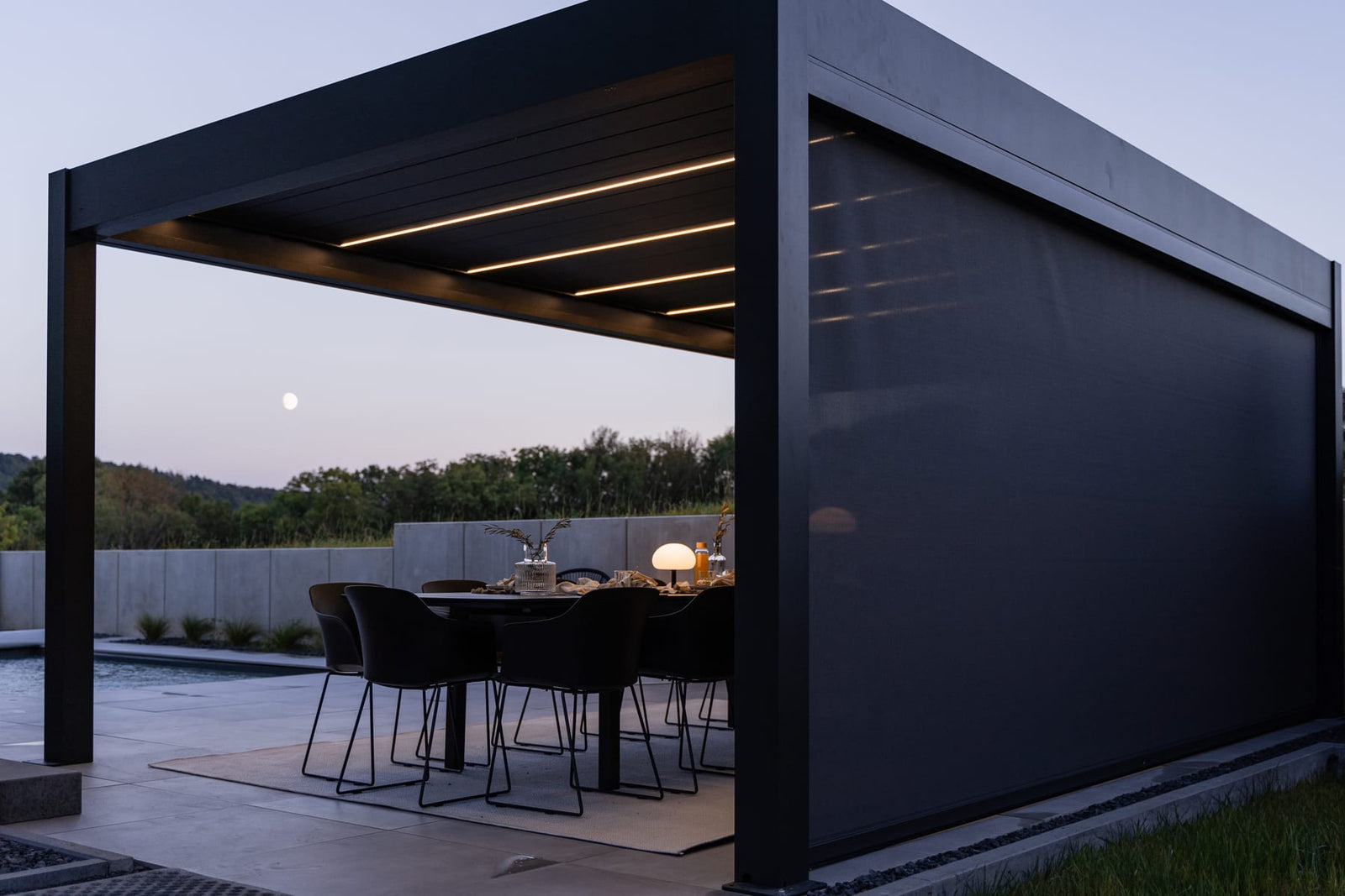 Famille réunie sous une pergola bioclimatique PERGOLUX en aluminium lors d'un dîner en terrasse, soirée d'automne éclairée